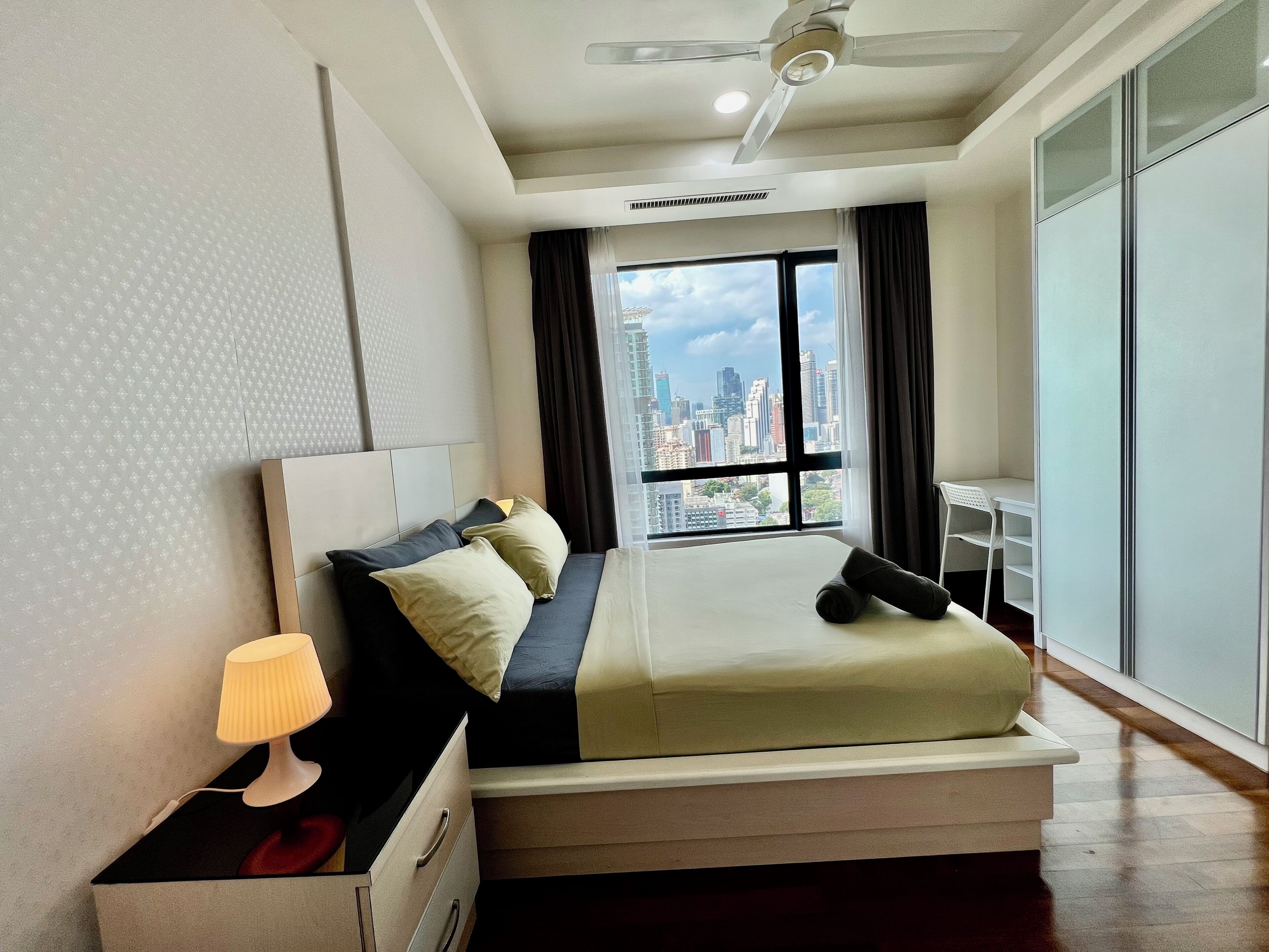 Ein Hotelzimmer mit Bett, Schreibtisch, Lampe und Blick auf die Stadt.
