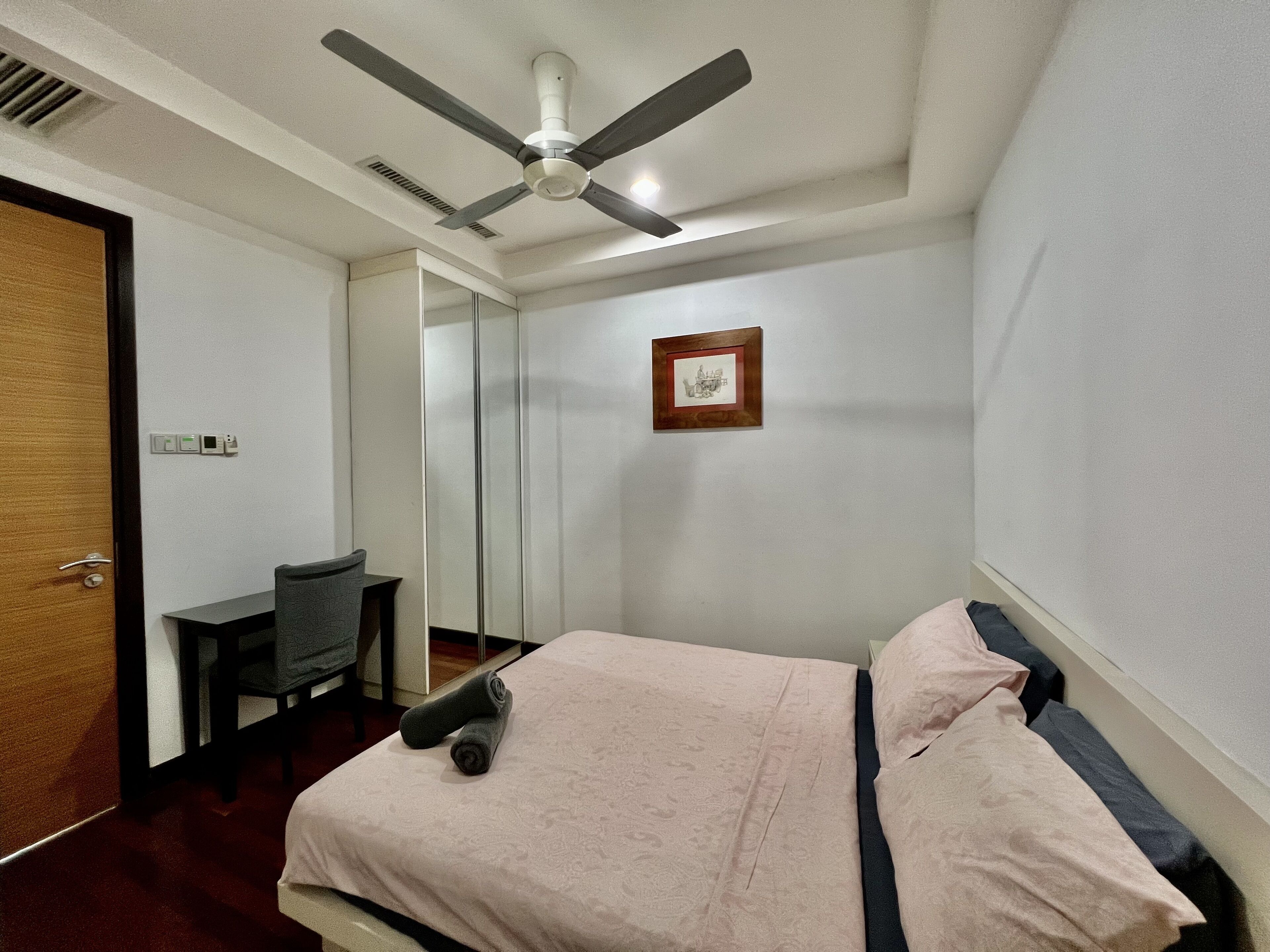 A hotel room with a bed, a desk, a chair, a ceiling fan, and a framed picture on the wall.