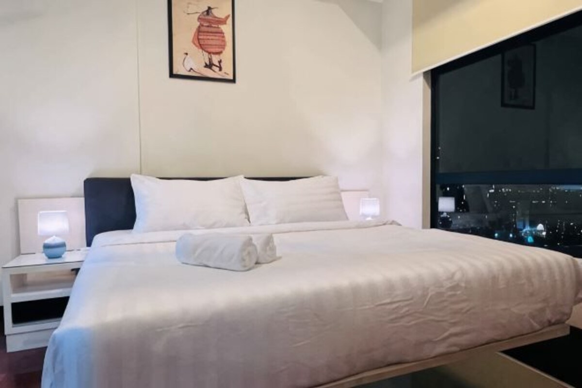 Una habitación de hotel moderna con una cama grande, mesitas de noche y vistas a la ciudad.