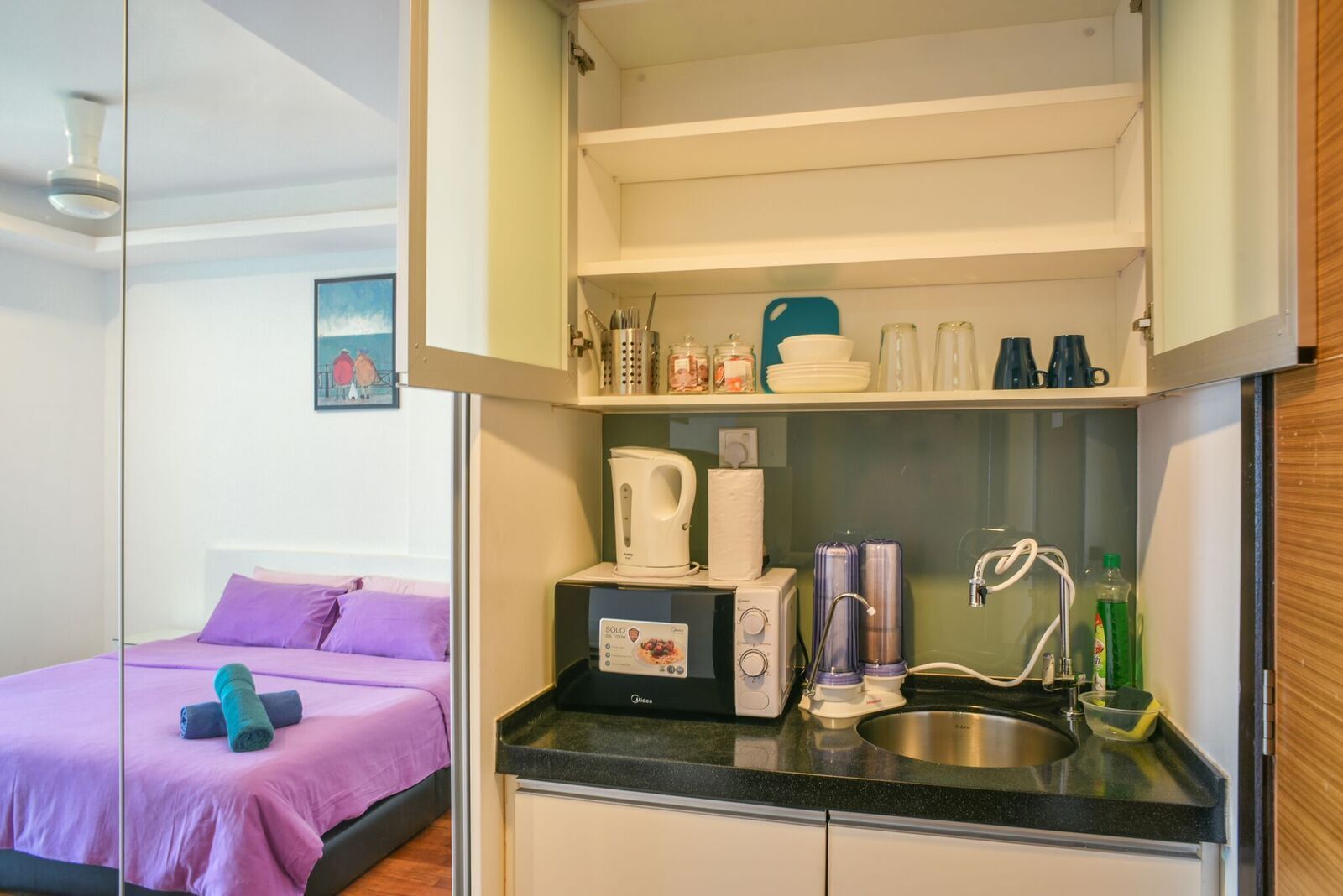A compact room with a bed, kitchenette, and a small bathroom.