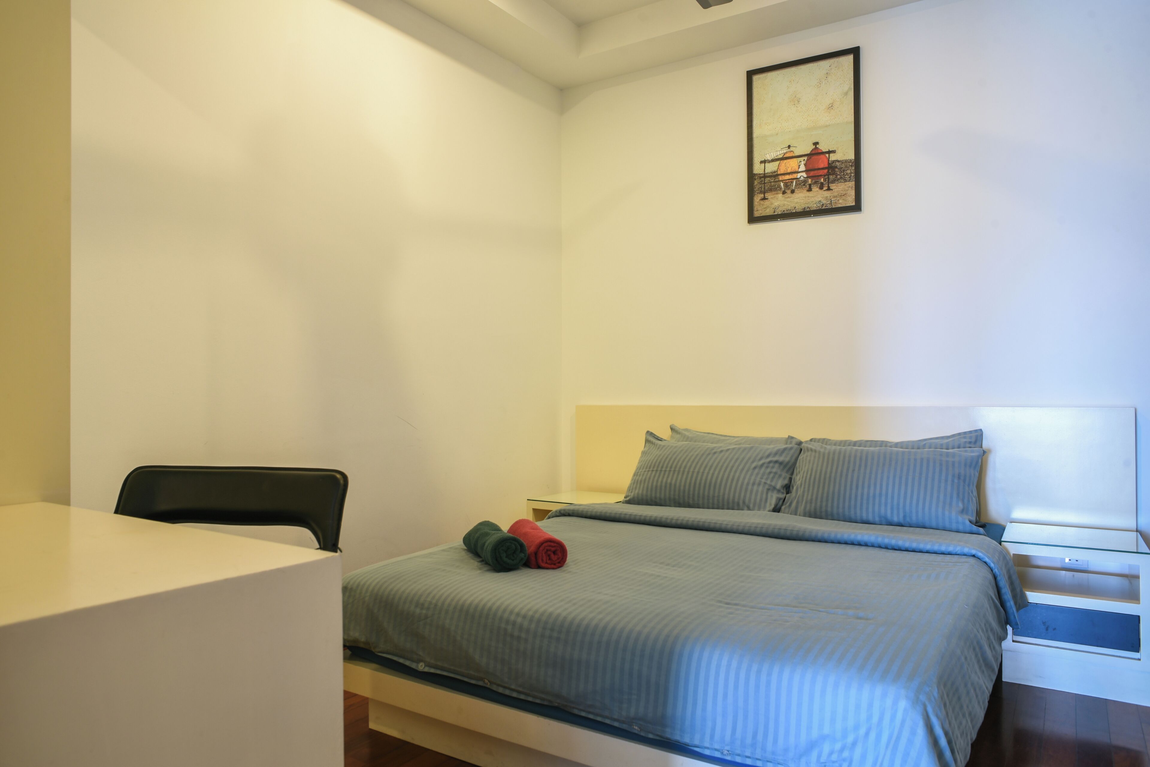 A bedroom with a bed, a chair, a bedside table, and a painting on the wall.