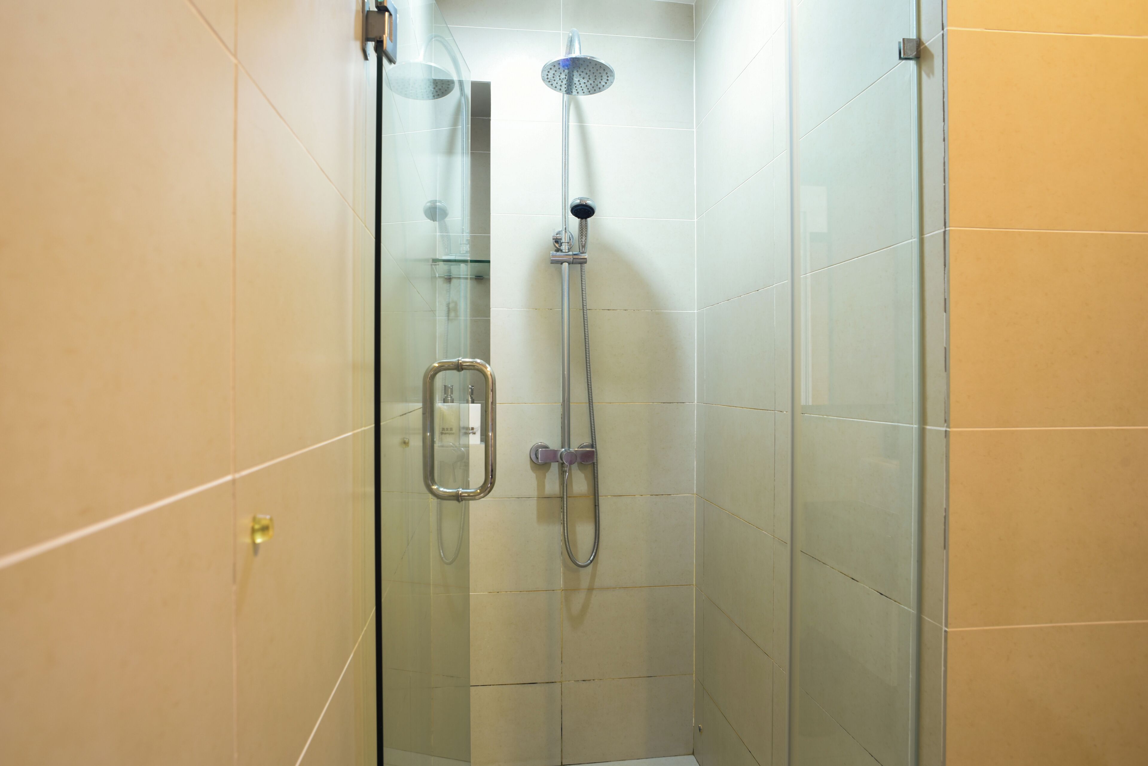 A glass-enclosed shower with a handheld showerhead and a wall-mounted faucet.