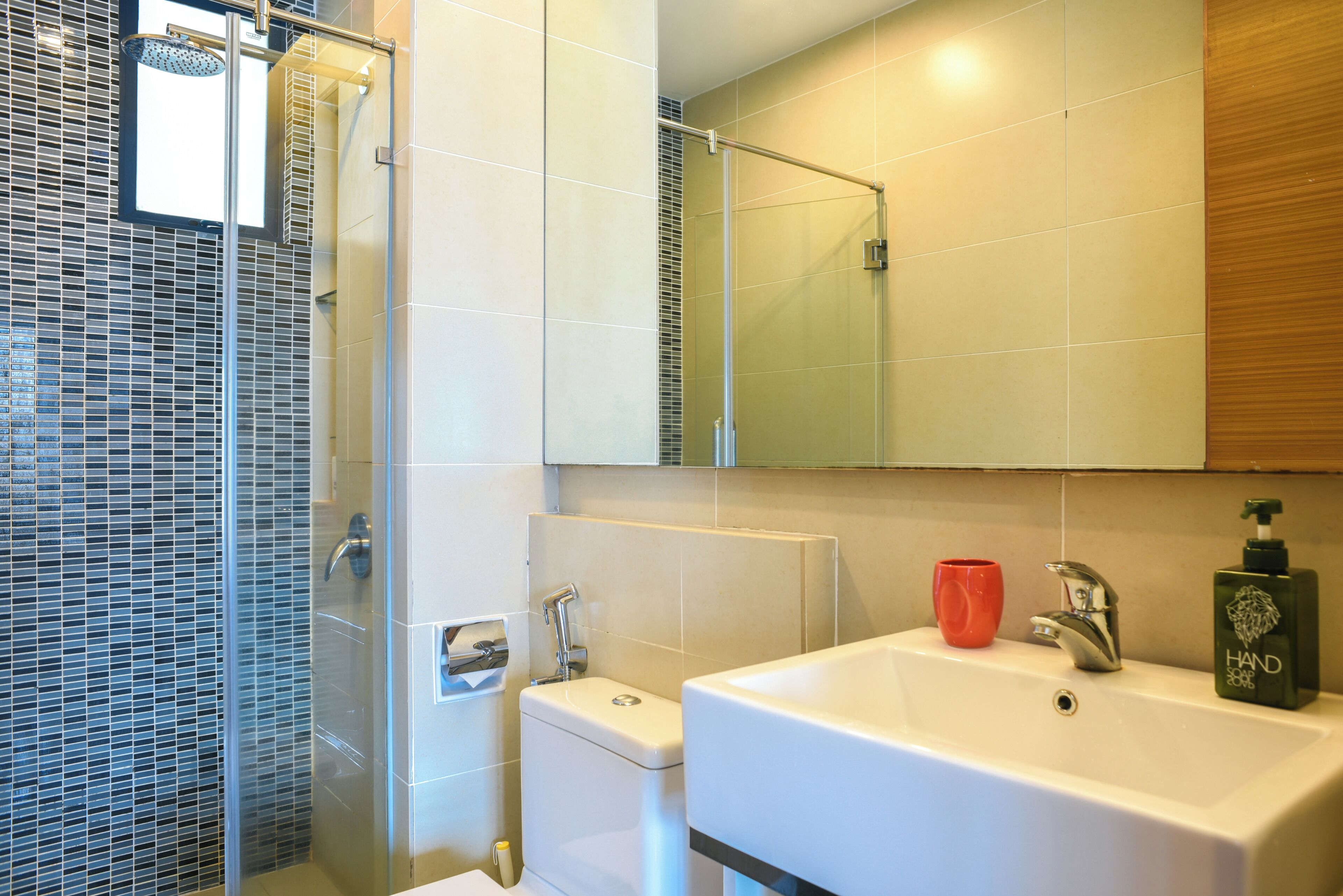 Une salle de bain avec une douche à parois de verre, des toilettes, un lavabo avec un miroir au-dessus, et une tasse rouge posée sur le lavabo.