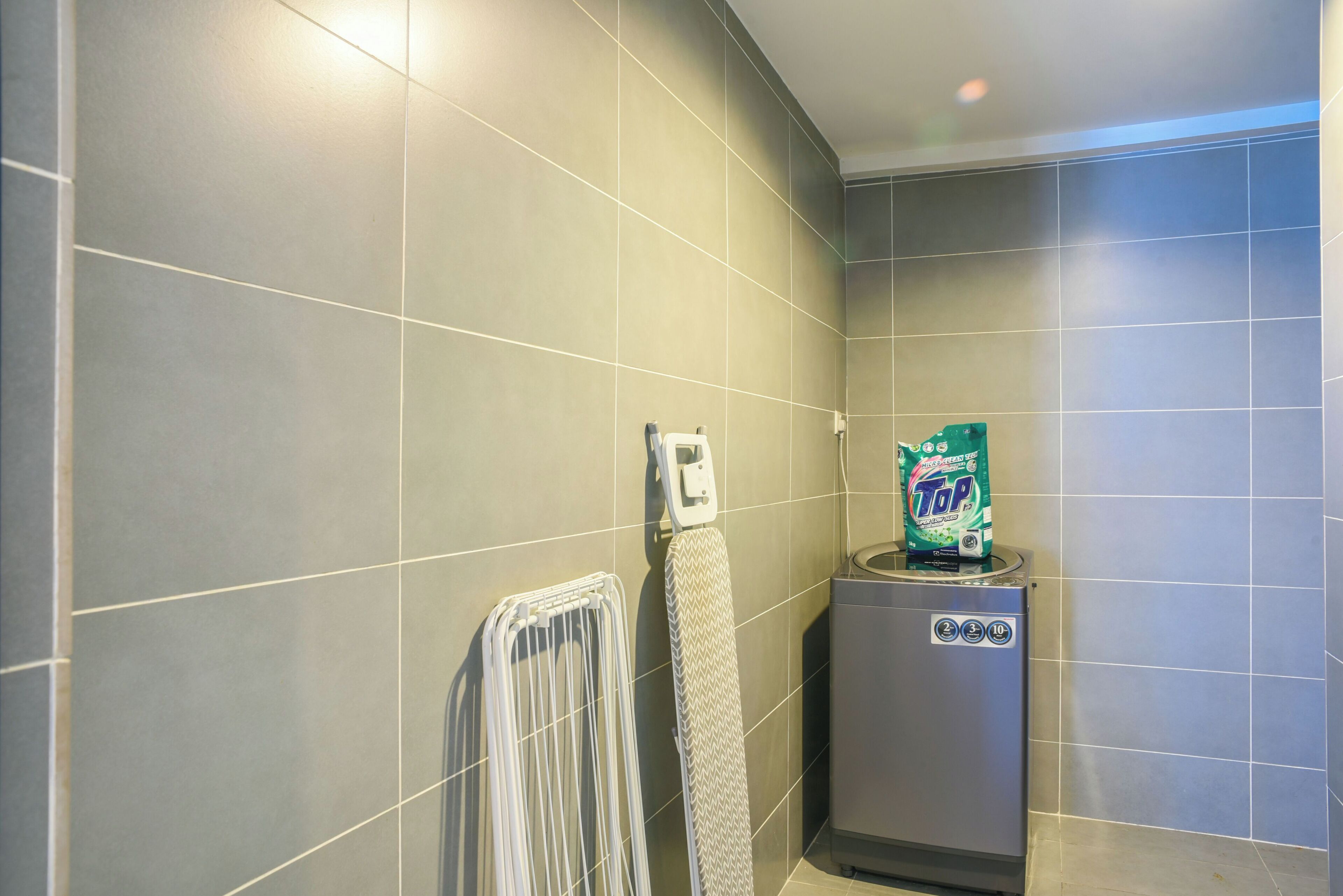 Un baño con paredes de azulejos grises, un perchero, un tendedero y un dispensador de jabón.