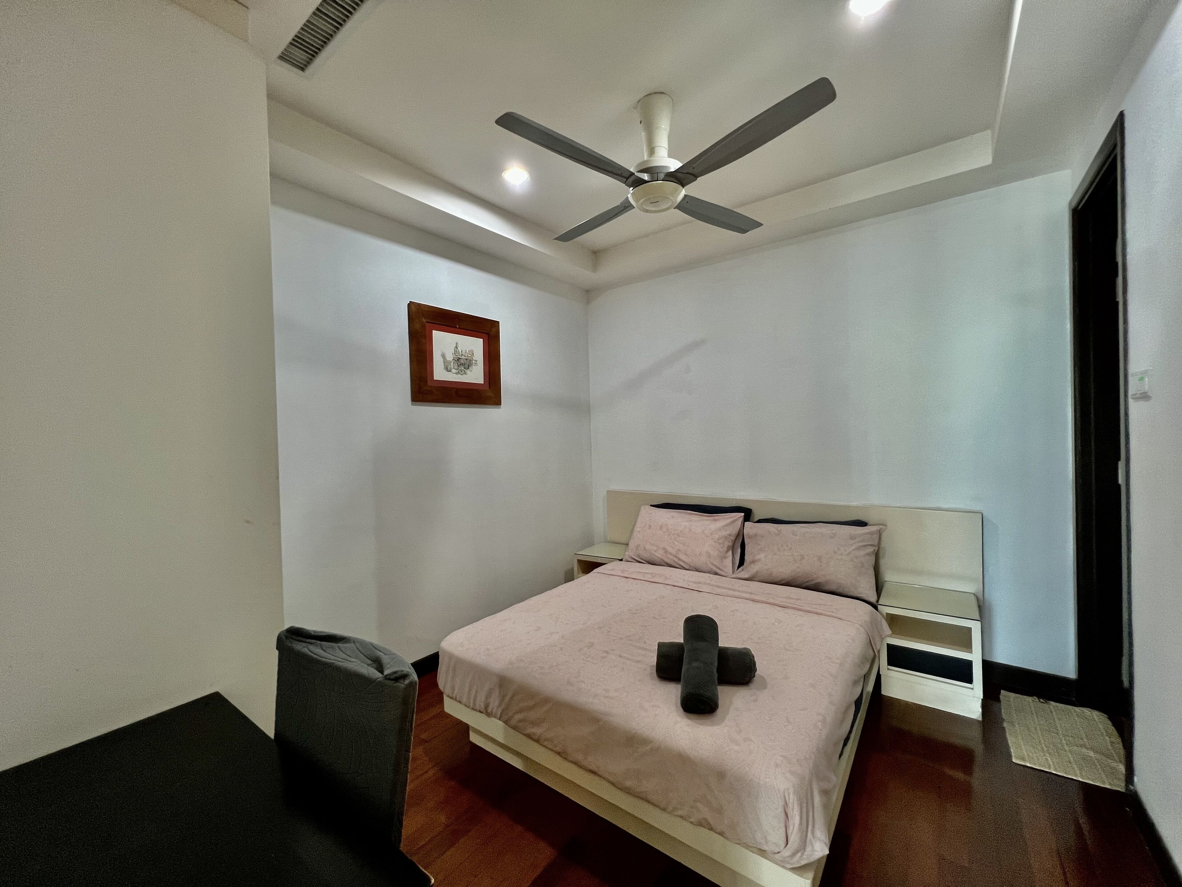Ein Schlafzimmer mit einem Bett, einem Deckenventilator, einem gerahmten Bild an der Wand und einem kleinen Nachttisch.