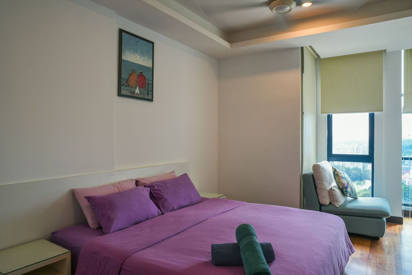 A bedroom with a large bed, a nightstand, a chair with a cushion, and a window with a view.
