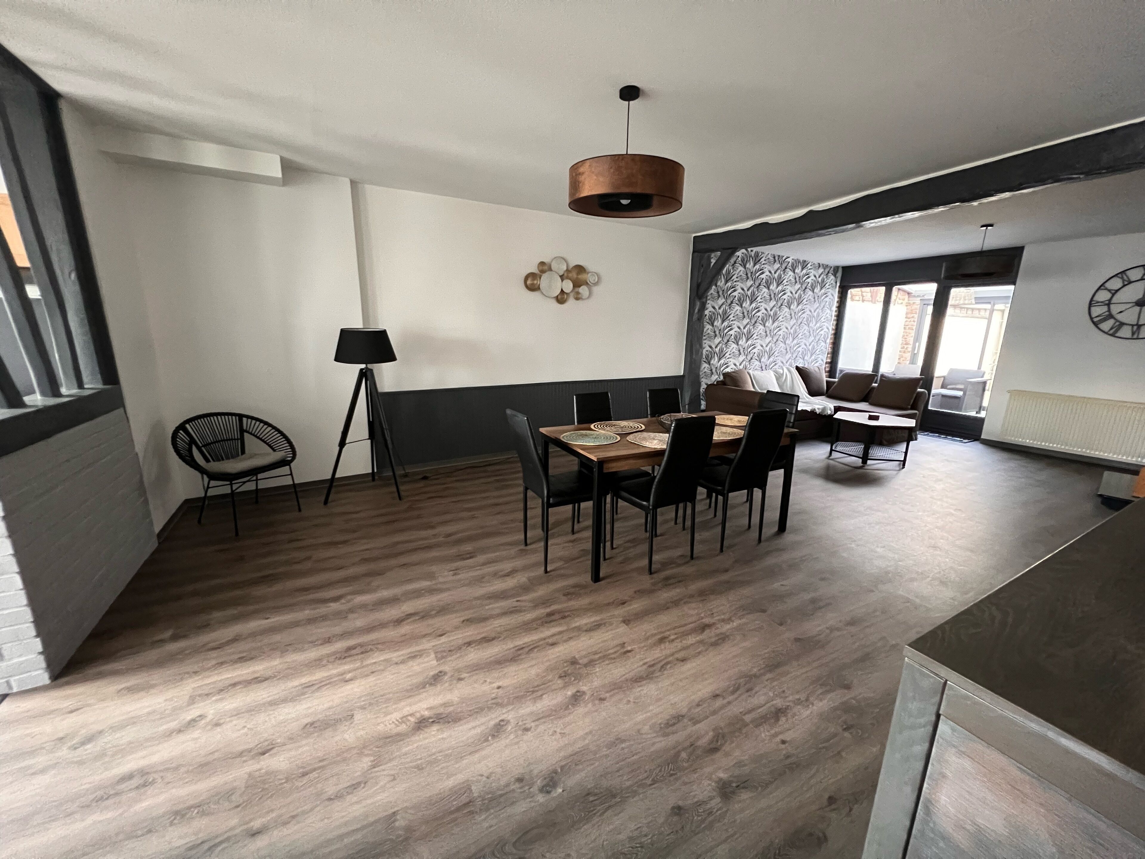 A modern dining area with a wooden table and chairs, a lamp, and a wall clock.
