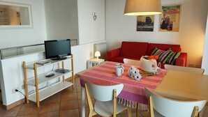 Una sala de estar moderna con un sofá rojo, una mesa de comedor con sillas, un televisor sobre un mueble bajo y una lámpara.