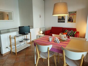 A modern living room with a red sofa, a dining table with chairs, a television on a stand, and a lamp. - A window 4 overlooking Lake Maggiore! (Stresa)