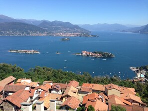 A coastal town with terracotta-roofed buildings, a marina with boats, and a backdrop of mountains. - A window 4 overlooking Lake Maggiore! (Stresa)