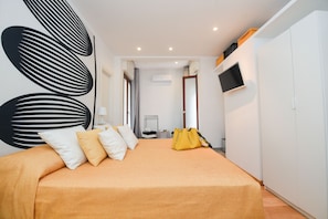 A bedroom with a bed, pillows, a TV, and an air conditioning unit.