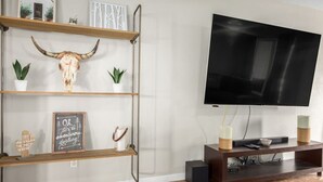 Ein Wohnzimmer mit einem Wand-Fernseher, Holzregalen mit Dekoration und einem Couchtisch.