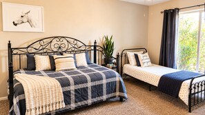 A bedroom with a large bed, a smaller bed, a potted plant, and a window with curtains.