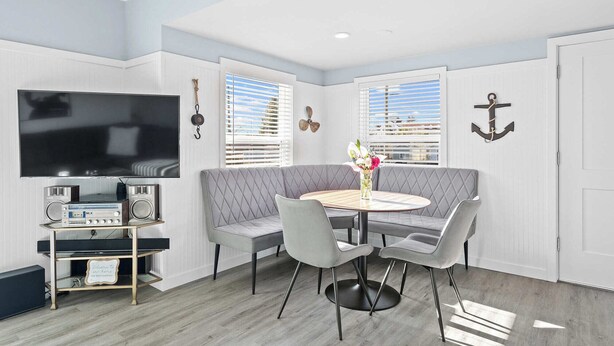 A modern living room with a grey upholstered sofa, a round wooden dining table with four chairs, a flat-screen TV mounted on the wall, and a small music player on a shelf. - Modern craftsman home close to all Garibaldi has to offer. Dog Friendly! (Rockaway Beach)