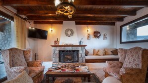 Ein gemütliches Wohnzimmer mit Kamin aus Stein, floralen Sesseln, einer Couch und einem an der Wand befestigten Fernseher.
