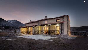 Ein Steinhaus mit Ziegeldach, einer überdachten Terrasse und Blick auf eine gebirgige Landschaft.