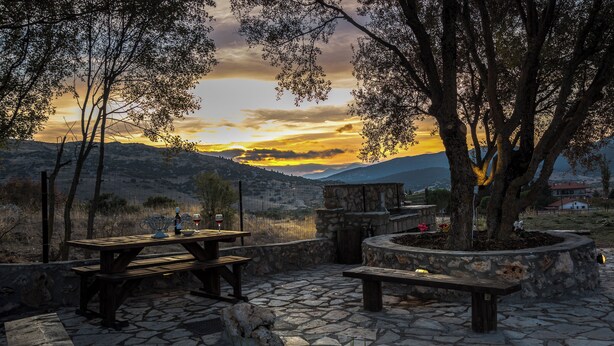 Eine Terrasse im Freien mit Steinböden, Holzbanken und einem Esstisch.