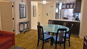A dining area with a glass table and chairs, a kitchen with stainless steel appliances, and a red armchair. -  -- RECENTLY REDUCED!! Marriott Grand Chateau---Great Formula 1 viewing Nov 2023 (Las Vegas)
