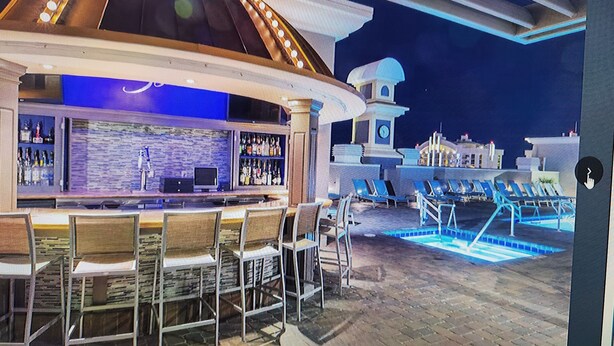 A bar area with a poolside view, including a bar counter, seating, and a pool. -  -- RECENTLY REDUCED!! Marriott Grand Chateau---Great Formula 1 viewing Nov 2023 (Las Vegas)