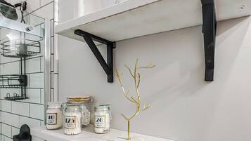 A bathroom with white tiled walls, a white shelf with jars, a white Buddha statue, and a potted plant.