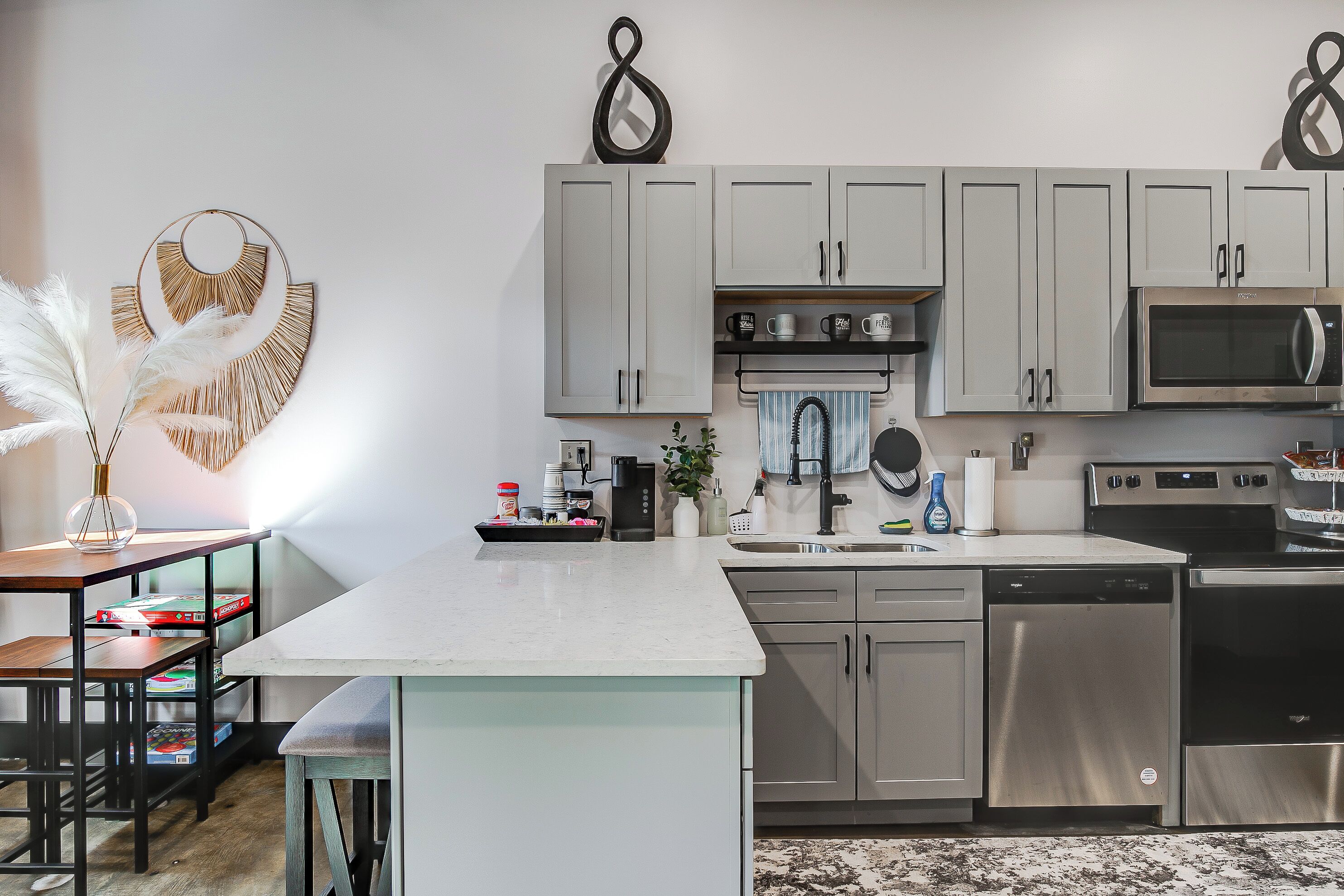 A modern kitchen with grey cabinets, stainless steel appliances, and a white countertop.