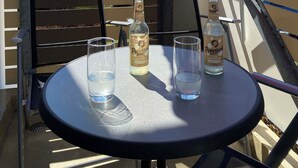A round table with two bottles of Proviant and two glasses of water, under a red umbrella, on a balcony with a view of buildings and trees.