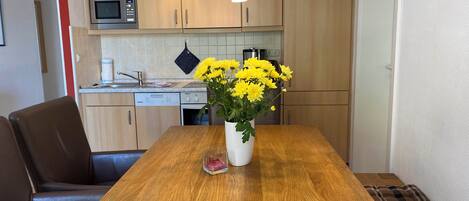 A modern kitchen with wooden cabinets, a built-in microwave, and a dining table with a vase of yellow flowers.