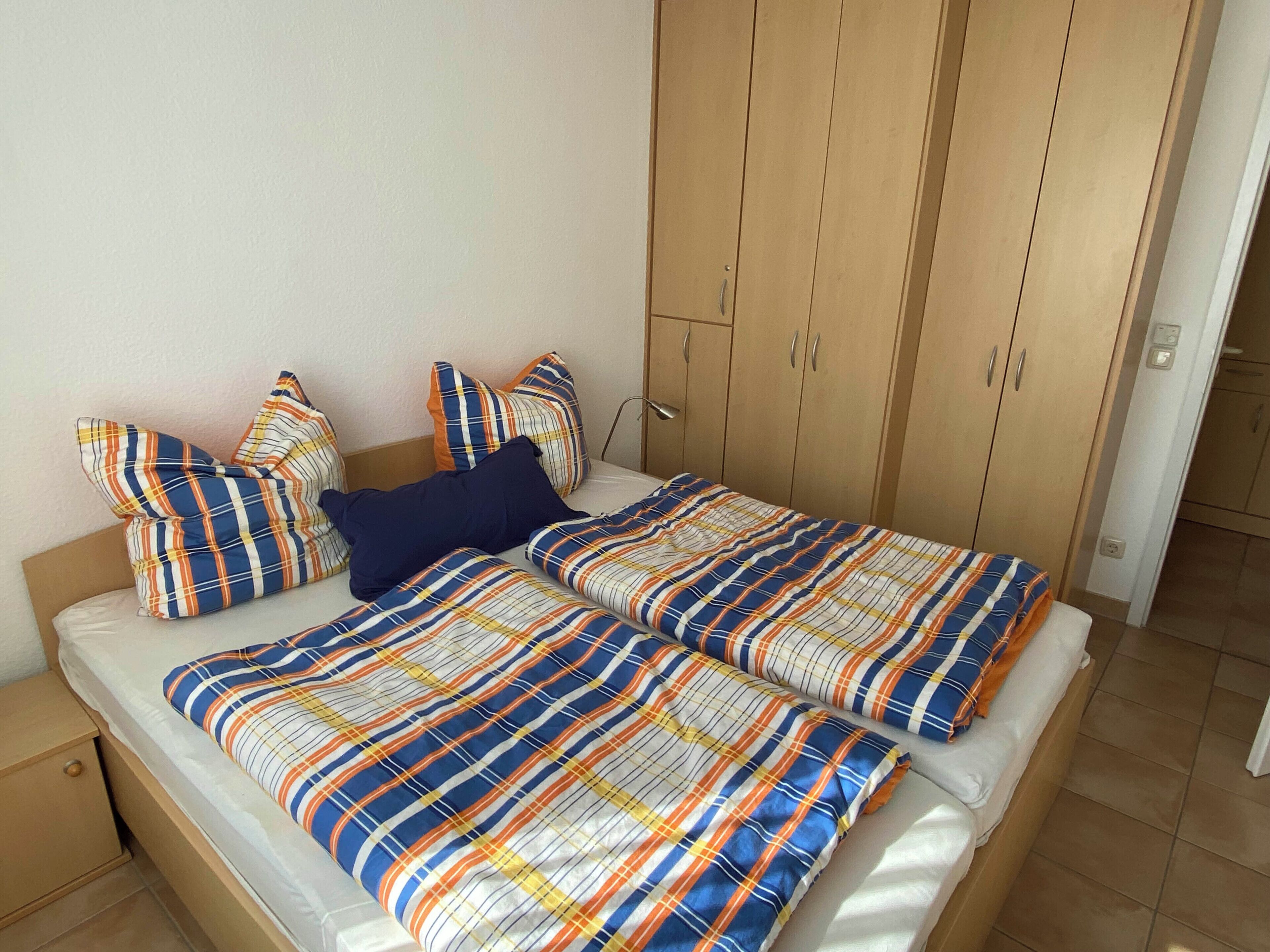Un dormitorio con cama, almohadas, armario y mesita de noche.