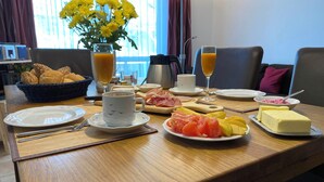 A breakfast table with plates of food, a coffee cup, a glass of orange juice, and a vase of yellow flowers.