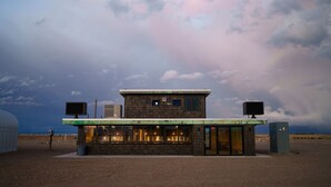 A small, standalone building with a flat roof, a single entrance, and two large screens mounted on the roof. - Frontier Drive Inn  (Center)
