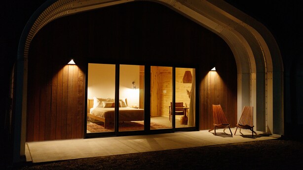 A modern hotel room with a large sliding glass door, a bed, a desk, and two chairs. - Frontier Drive Inn  (Center)