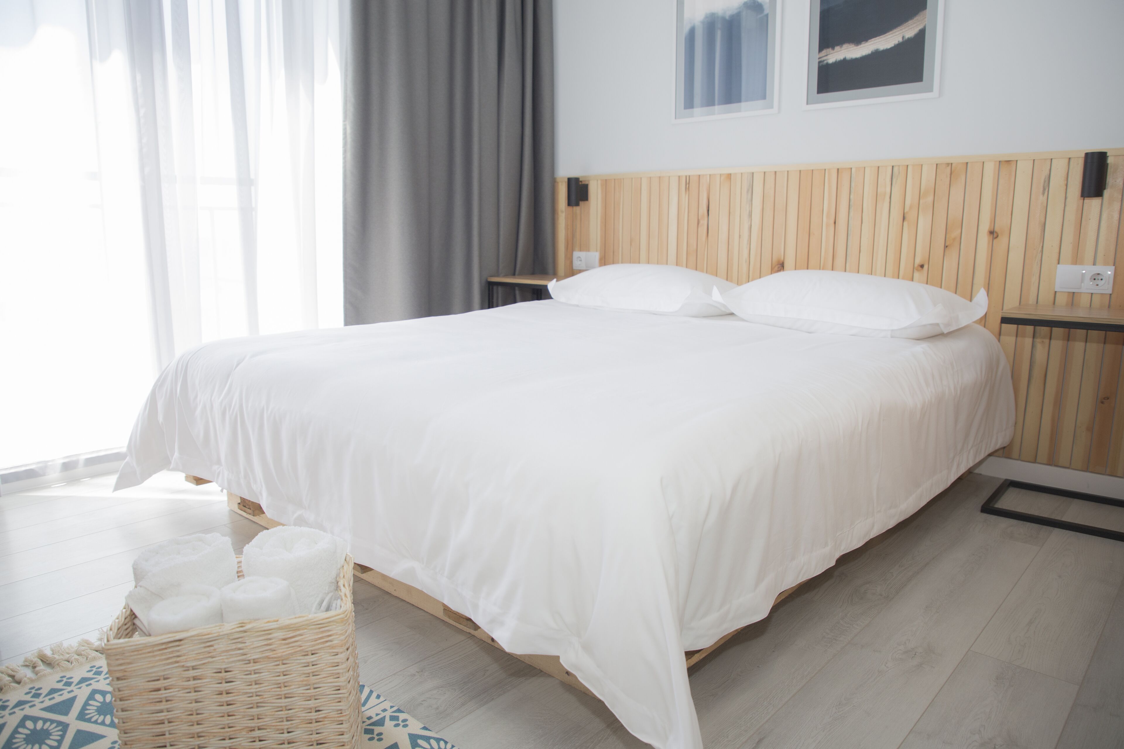 Een net opgemaakt bed met witte lakens, een houten hoofdbord en een klein nachtkastje met een lamp.