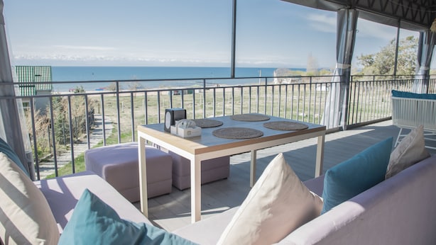 A balcony with a view of the sea, a table with placemats, and cushioned seating. - Silence hotel (Cholpon-Ata)