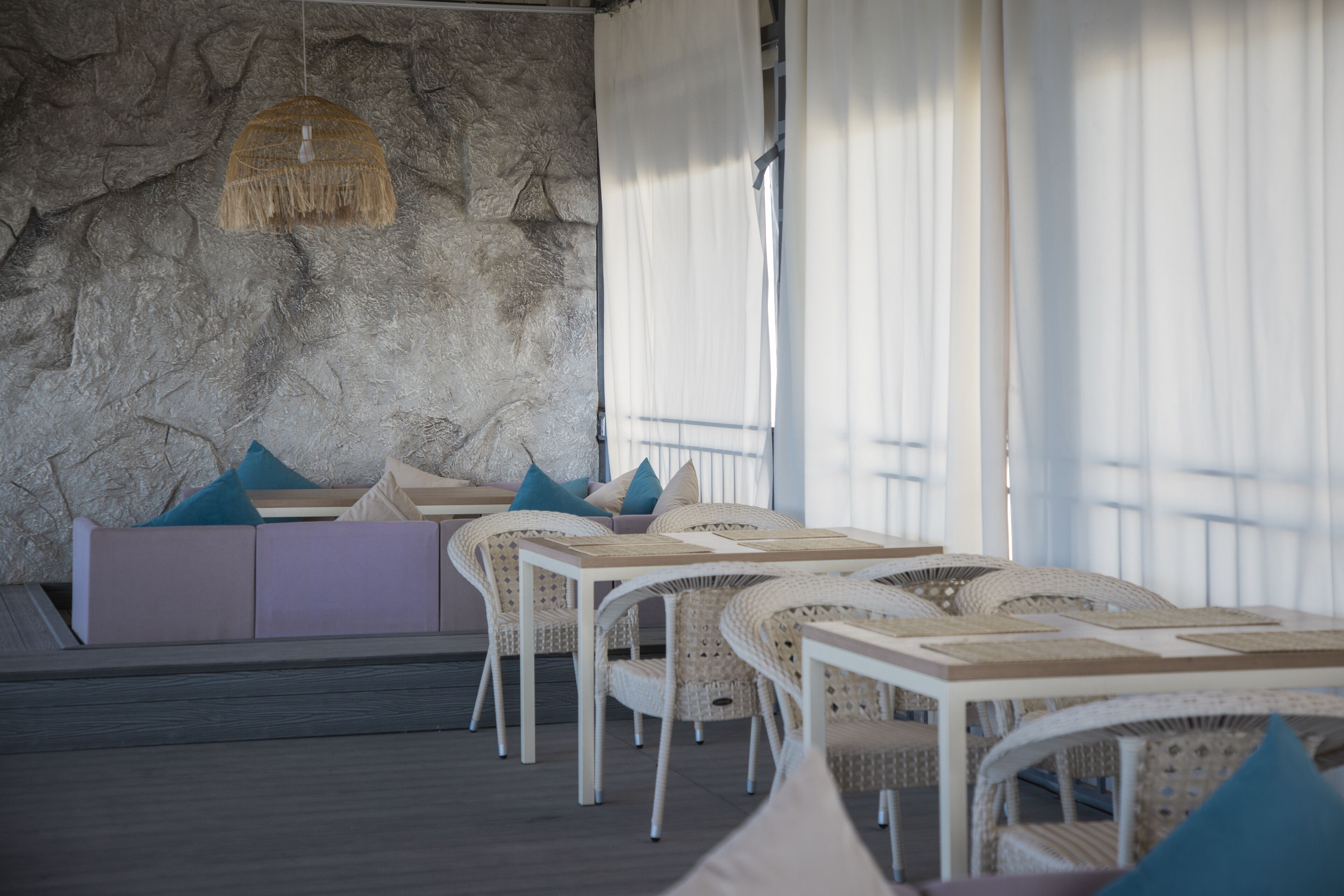 A modern dining area with white wicker furniture, a stone wall, and a view of the outdoors.