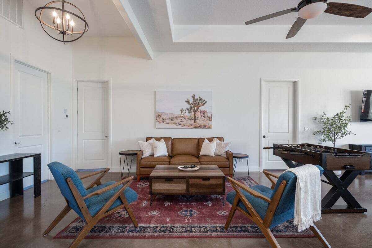 A living room with a brown leather sofa, blue armchairs, a wooden coffee table, and a red patterned rug.
