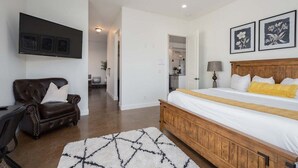A bedroom with a bed, a brown leather sofa, a TV mounted on the wall, and a ceiling fan.