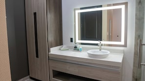 A bathroom with a white sink, a mirror with a light, and wooden cabinets. - Comfeeni Inn and Suites (South Houston)