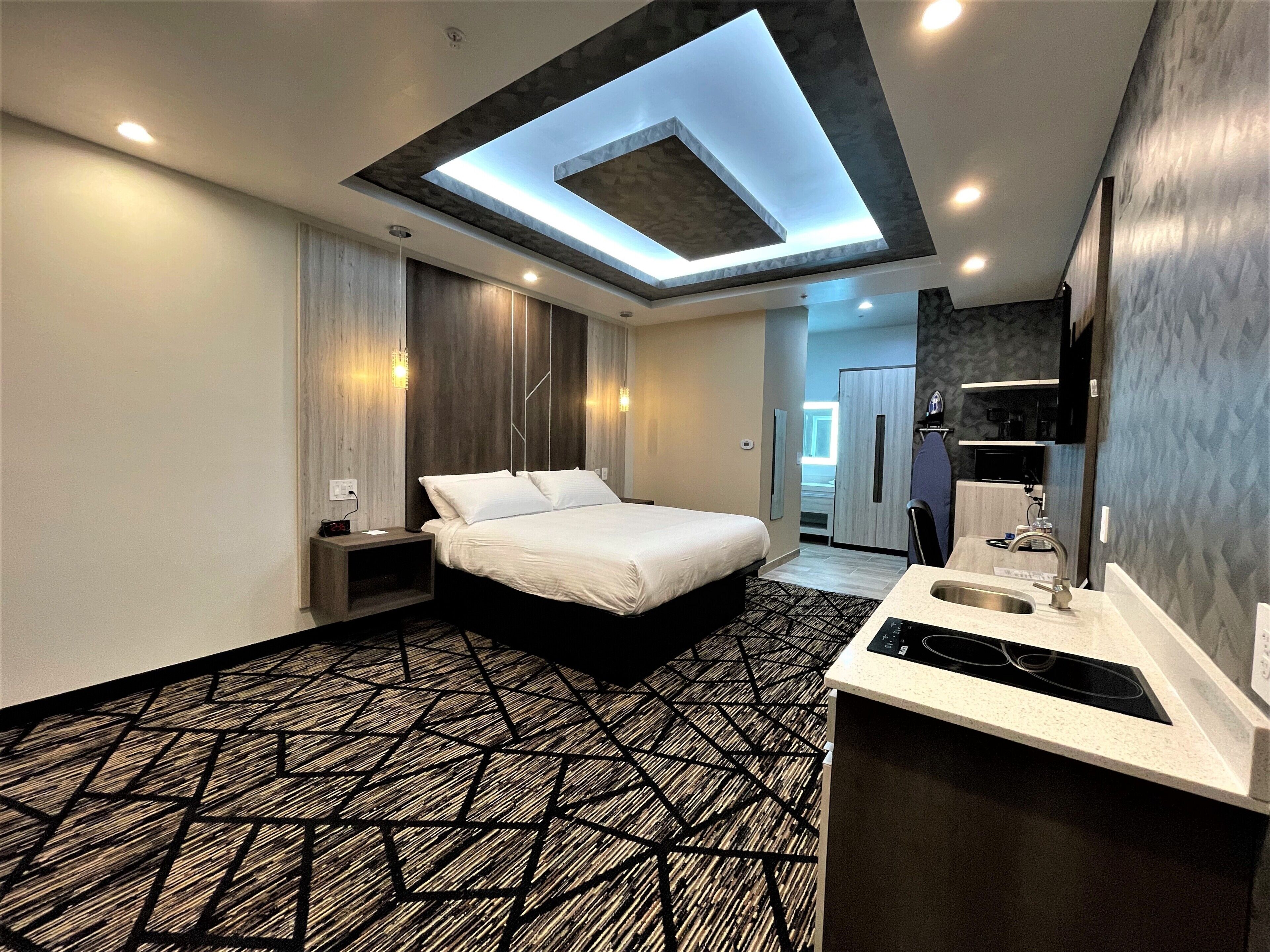 A modern hotel room with a bed, a built-in desk with a sink, and a skylight above the bed.