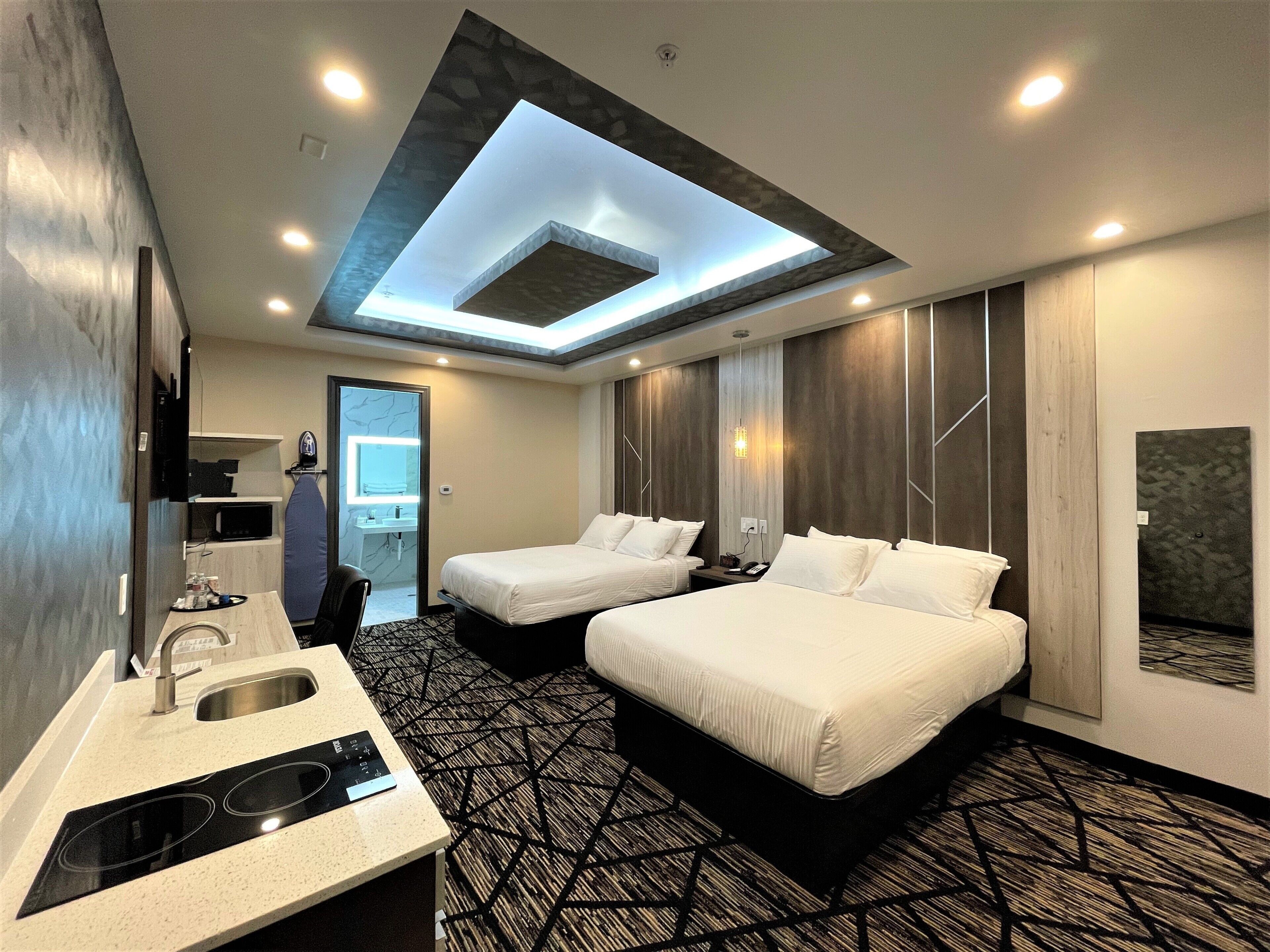Een moderne hotelkamer met twee bedden, een dakraam, een badkamer met spiegel en een kitchenette.