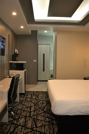 A hotel room with a bed, a desk with a chair, a television, and a microwave.