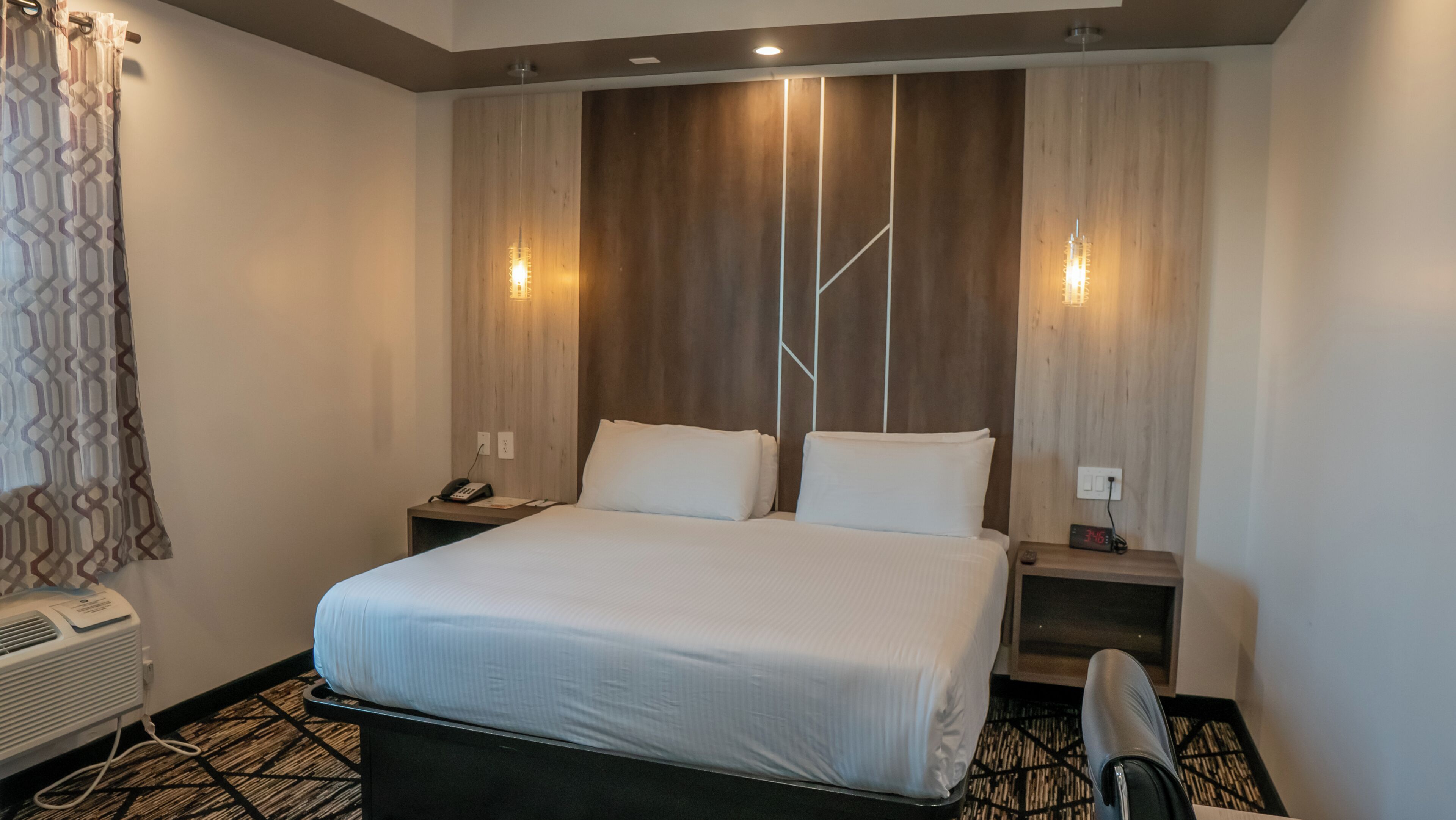 A hotel room with a bed, two bedside tables, a heater, and a clock.