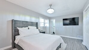 A modern bedroom with a large bed, a ceiling fan, a flat-screen TV, and a walk-in closet. - ***Spacious 4 Bedroom home w 1.1 acre backyard 10 mins Airport*** (atlanta)