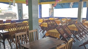 A dining area with wooden tables and chairs, a tiled floor, and a view of the sea through large windows. - Playa El Obispo  C  La Marea La Libertad (La Libertad)