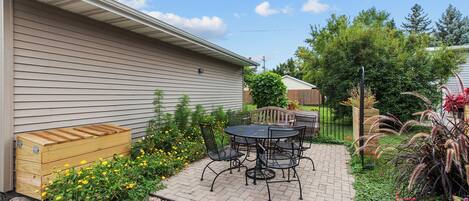 A patio with a table and chairs, a wooden bench, and a small garden with flowers and shrubs.