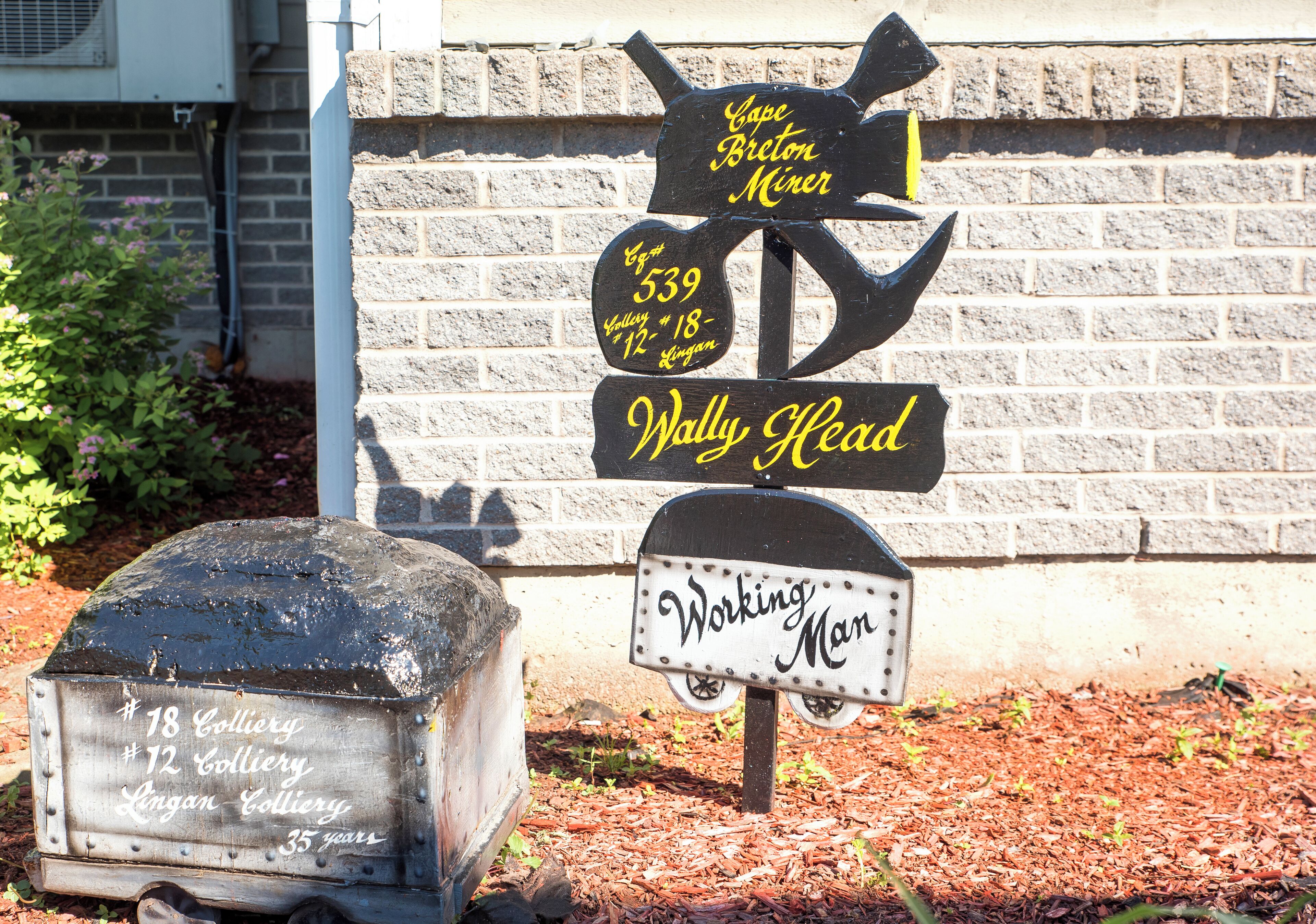Une plaque en métal noir avec des lettres jaunes indiquant les directions vers « Cape Breton Miner » et « Wally Head ».
