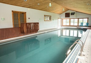 A large indoor swimming pool with wooden beams on the ceiling, a wooden bench along the pool, and large windows providing natural light. - Rita’s Retreat Main House ~ Indoor Saltwater Pool ~ with Lake View! (Sydney)