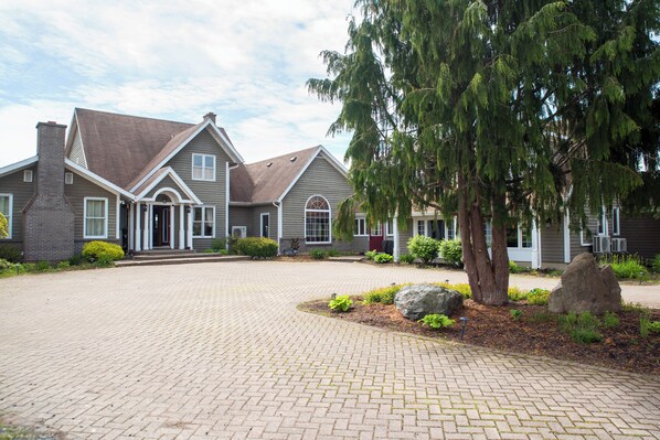 A two-story house with a brick driveway and a large tree in the front yard. - Rita’s Retreat Main House ~ Indoor Saltwater Pool ~ with Lake View! (Sydney)