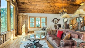 A rustic interior with wooden beams, a leather sofa, a glass coffee table, and a cowhide rug. - Bozeman Cabin: Deck w/ Jacuzzi & Gas Grill! (Bozeman)