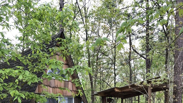 Una cabaña rústica con terraza de madera, un espacio al aire libre cubierto para sentarse y una chimenea de piedra.