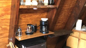 Una cocina compacta con refrigerador, cafetera y una alacena con frascos y tazas.